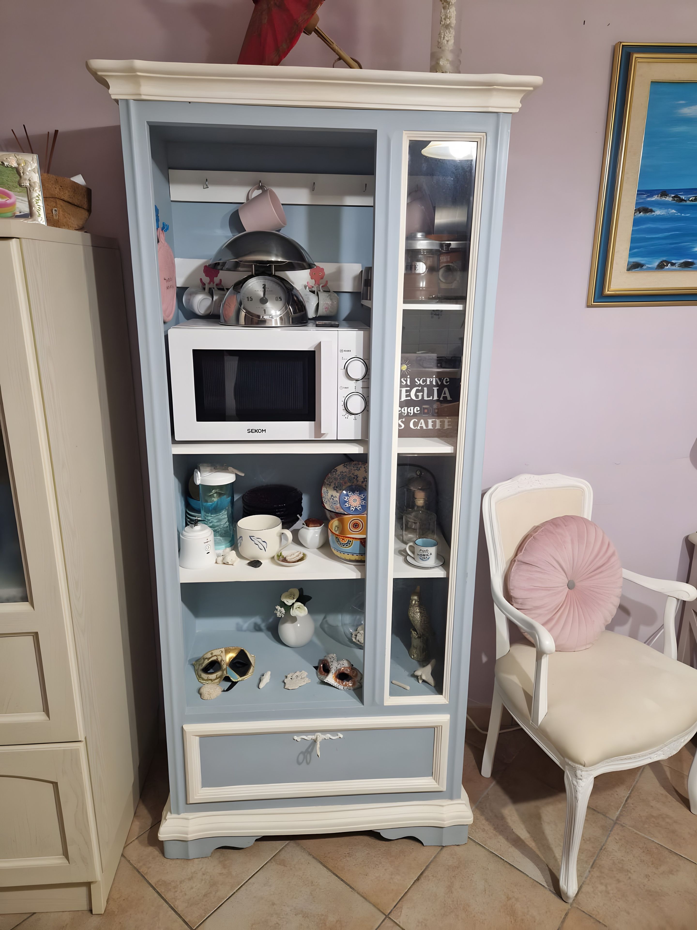 Un mobiletti blu con un forno a microonde, un set da tè e oggetti decorativi.