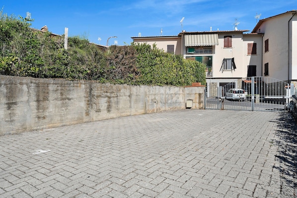 Un patio empedrado con un muro de concreto, una verja de metal y un edificio con techo de tejas al fondo.