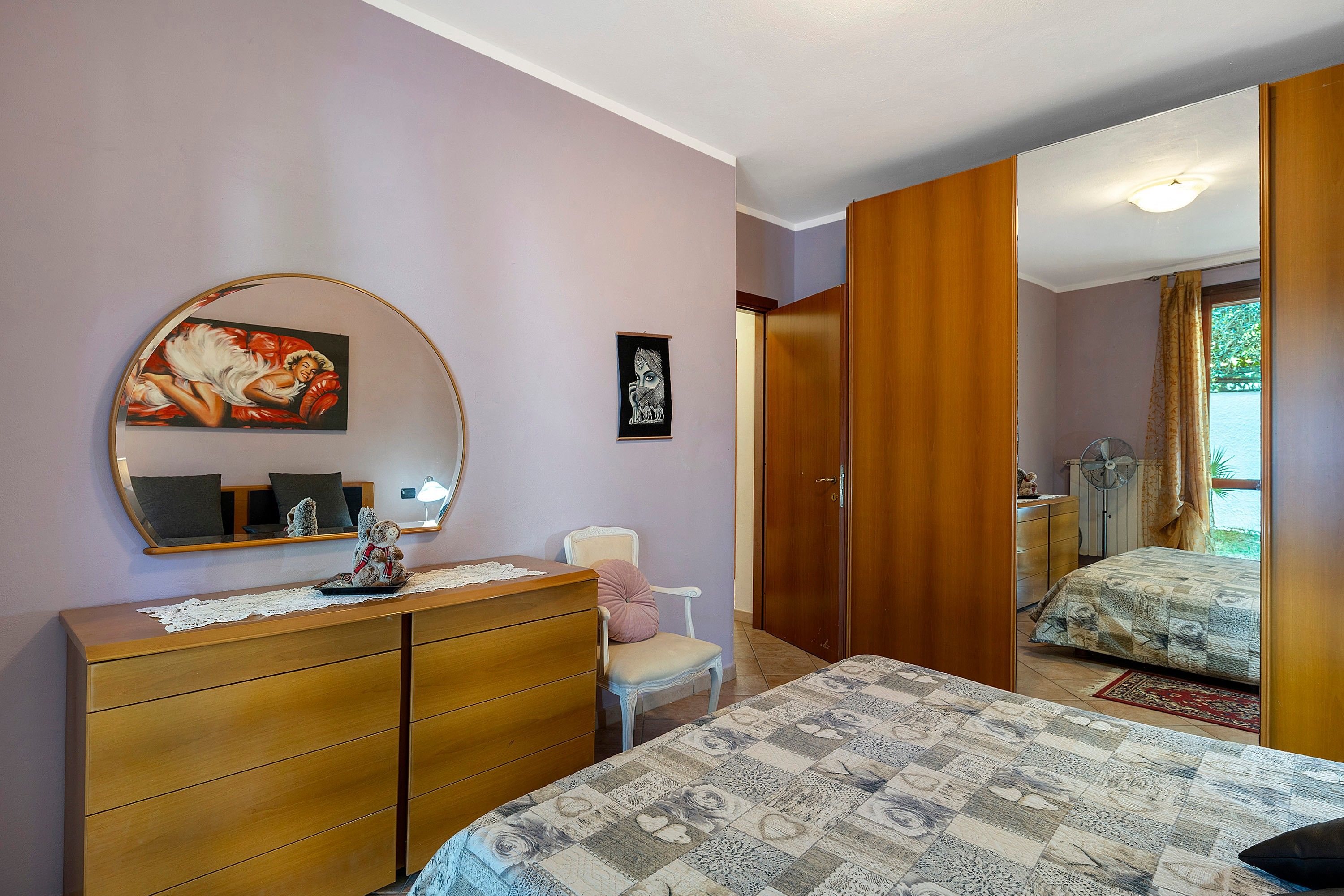 A bedroom with a bed, dresser, mirror, and a door leading to another room.