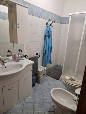 Ein Badezimmer mit Waschbecken, Spiegel, Bademantel und Duschbereich.