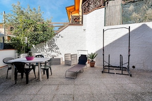Un patio exterior con una mesa y sillas, un rincón de descanso y una planta trepadora.