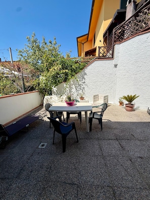 Eine Terrasse mit Tisch und Stühlen, umgeben von Kübelpflanzen und einer weißen Mauer.