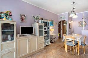 Un área de comedor con una mesa y sillas, un televisor sobre un mueble, y varios objetos decorativos en las paredes.