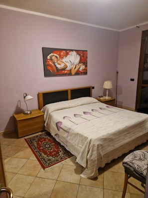 Ein Schlafzimmer mit einem Bett, Nachttischen, einer Lampe, einem Gemälde und einem gemusterten Teppich.