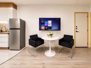 A modern kitchen with a built-in refrigerator, a flat-screen TV mounted on the wall displaying streaming services, two black chairs around a white table, and a wooden door. - Coco 1&2 · Two suites with terrace in Condesa · 2 baths (Ciudad de México)