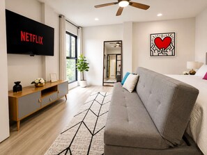 A modern hotel room with a grey sofa, a flat-screen TV, a ceiling fan, and a large window. - Coco 1&2 · Two suites with terrace in Condesa · 2 baths (Ciudad de México)