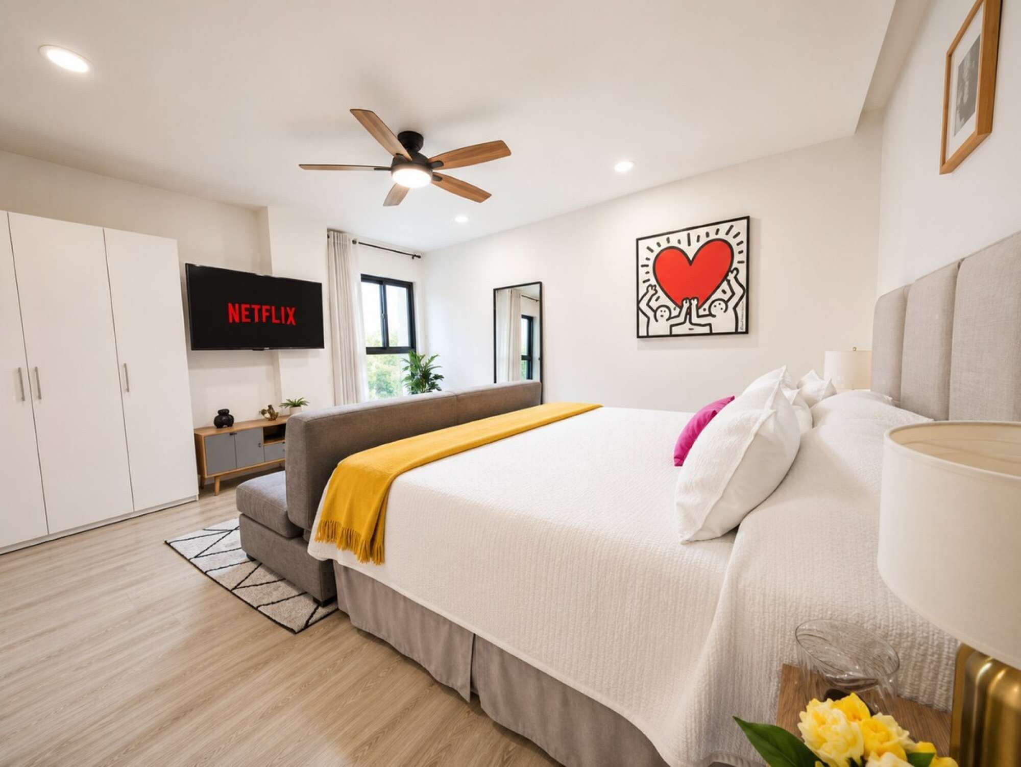 Une chambre moderne avec un lit, un téléviseur, un ventilateur de plafond et une œuvre d’art murale.