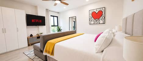 A modern bedroom with a bed, a TV, a ceiling fan, and a wall art piece.
