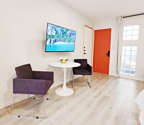 A modern room with a flat-screen TV on the wall, two chairs, a small round table, and a door with an orange accent. - Coco 4&5 · Two suites with terrace in Condesa · 2 baths (Ciudad de México)