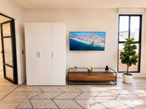 A room with a white wardrobe, a flat-screen TV mounted on the wall, a glass coffee table with decorative items, a potted plant, and a geometric-patterned rug. - Coco 7&8 · Two suites with terrace in Condesa · 2 baths (Ciudad de México)