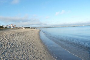 A beach with a pier extending into calm waters, a lighthouse, and buildings in the background. - Apartment 1 in the Hügel building (Ostseebad Binz)