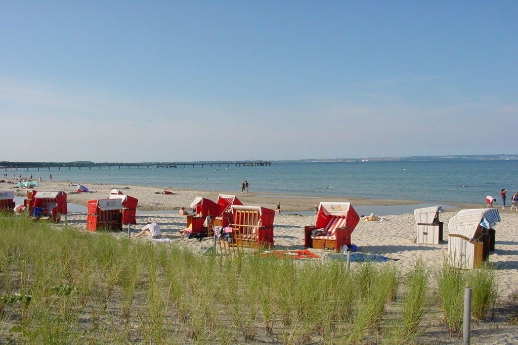 Een strand met rode strandhuisjes en een pier op de achtergrond.