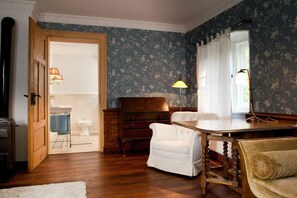 A room with a wooden floor, a white chair, a wooden desk, a lamp, and a window with curtains. - Old Forester's Lodge Hohnstein (Hohnstein)