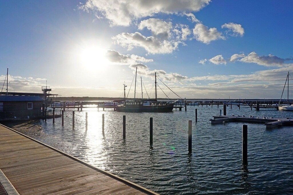 A wooden dock extending into calm water with a boat docked at the pier, surrounded by a clear sky.