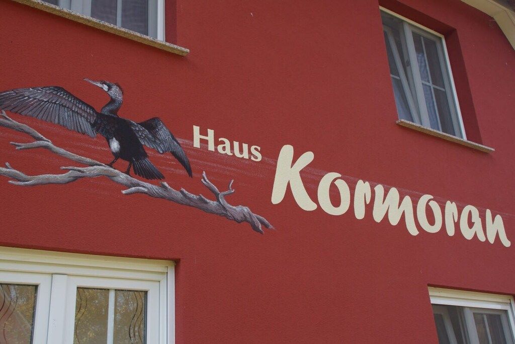 Un bâtiment à la façade rouge sur laquelle est peint le nom « Haus Kormoran ».