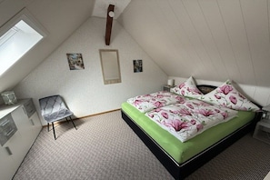 A bedroom with a bed, a chair, a desk, and a window.