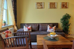 A living room with a sofa, a wooden dining table with a bowl of flowers, and a potted plant. - Holiday apartment in Waren with swimming pool (Waren)