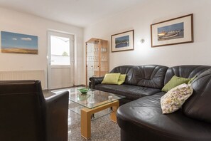 A living room with a leather sofa, glass coffee table, and a bookshelf. - House Hill Apartment 3 (Ostseebad Binz)