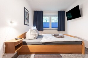 A bedroom with a bed, bedside table, lamp, and a window with curtains. - House Hill Apartment 3 (Ostseebad Binz)