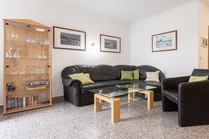 A living room with a black leather sofa, a glass coffee table, and a wooden bookcase with glassware. - House Hill Apartment 3 (Ostseebad Binz)