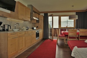 Eine moderne Küche mit Holzschränken, einem eingebauten Ofen und einem roten Teppich, der zu einem Essbereich mit Tisch und Stühlen führt.