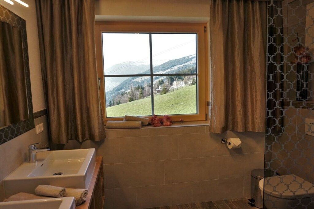 Un baño con un ventanal amplio, un lavamanos, un inodoro y una zona de ducha.