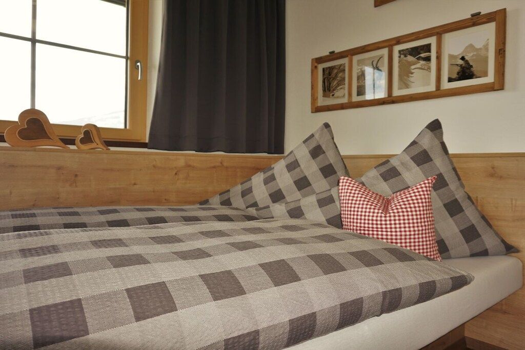Un lit avec une couvre-lit à carreaux, une tête de lit en bois et une fenêtre avec des rideaux.