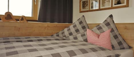 A bed with a checkered bedspread, a wooden headboard, and a window with curtains.