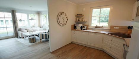 A modern kitchen with white cabinetry, a clock on the wall, and a window providing natural light.