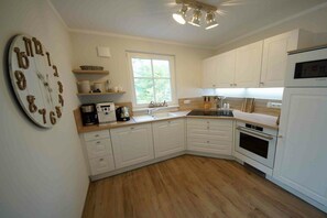 A kitchen with white cabinets, a wooden countertop, a built-in oven, and a clock on the wall. - Holiday home in Prerow with sauna (Prerow)