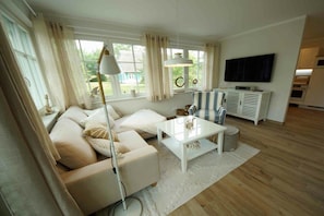 Ein Wohnzimmer mit einer Couch, einem Couchtisch, einer Lampe, einem Fernseher und Blick ins Freie.