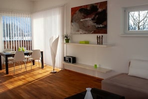Ein modernes Wohnzimmer mit Essbereich, einem großen abstrakten Gemälde und Blick ins Freie.