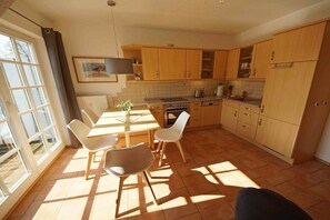 Een keuken met houten kastjes, een eettafel met stoelen en een raam met gordijnen.
