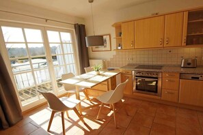 A kitchen with a dining table and chairs, a television mounted above the counter, and a view through the window. - Holiday apartment with 2 bedrooms (Prerow)