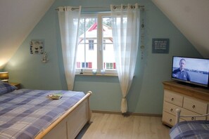 Ein Schlafzimmer mit einem Bett, einem Fernseher, einem Fenster mit Vorhängen, einem Schminktisch und einer Wandplatte.