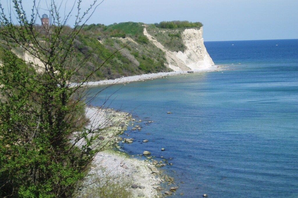 Un paisaje costero con un acantilado, mar azul cristalino y vegetación escasa.