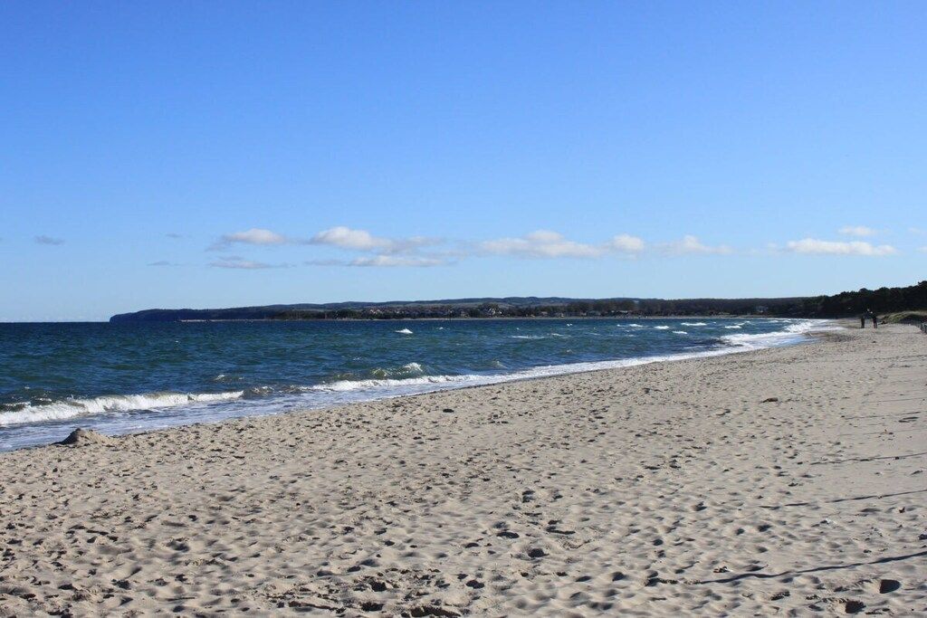 Een strand met een heldere lucht, golven en een landmassa in de verte.