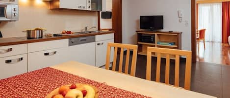 A modern kitchen with a dining area, a television, and a red patterned tablecloth.