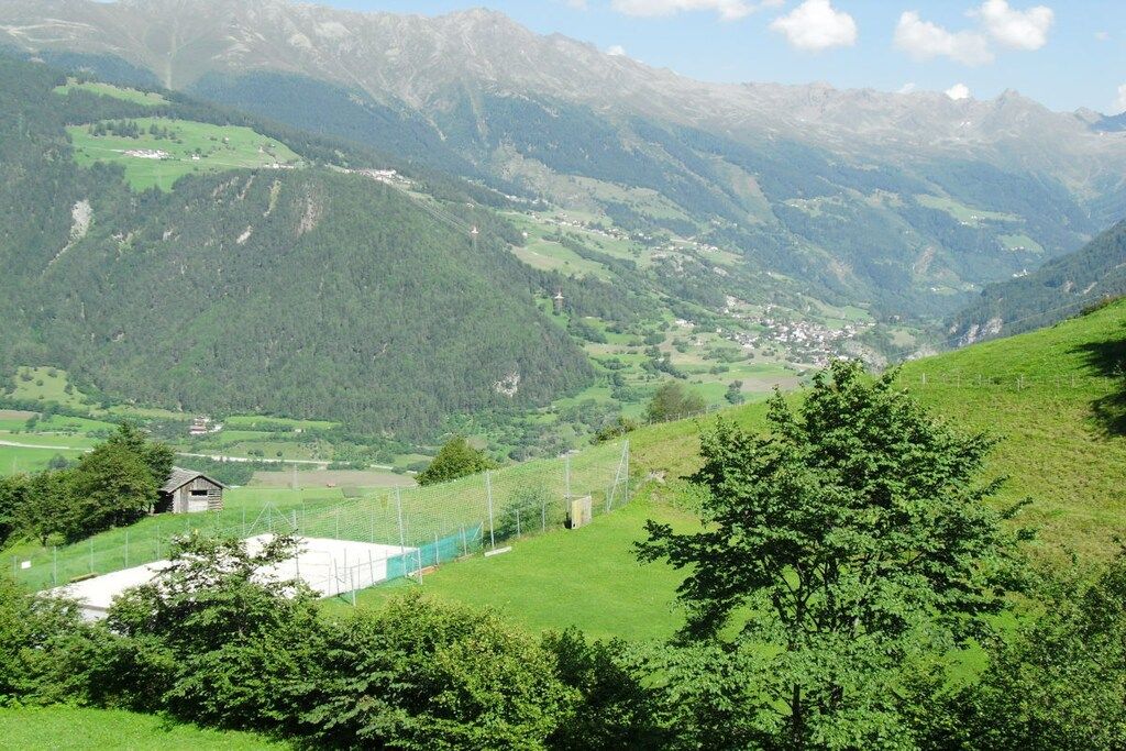 A mountainous landscape with a small building and a fenced area, likely a farm or vineyard.