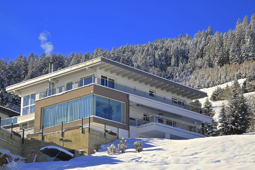 A modern multi-story building with large windows and balconies, surrounded by a snowy landscape and trees.