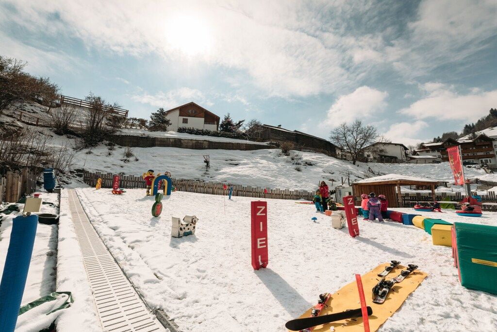 A snowy ski slope with a wooden fence, a sled, and a ski lift in the background.