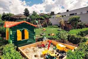 Ein Kinderspielbereich mit einem kleinen Haus, einer Rutsche und verschiedenen Spielzeugen.