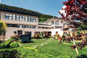 Un edificio moderno con varios pisos, un césped bien cuidado y una zona de juegos.