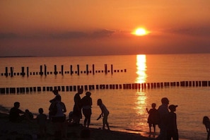 Ein Sonnenuntergang über ruhigem Wasser, am Ufer befinden sich Personen.