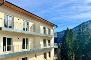 A multi-story building with balconies, large windows, and a mountainous backdrop. - Schuster's Alpine Panorama (Seewiesen)