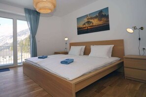 A modern bedroom with a wooden bed, a painting of a sunset, and a view through the window.