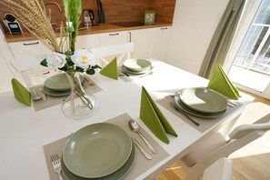 A dining table set with green plates, silverware, and a vase with white flowers.
