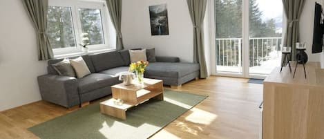 Een moderne woonkamer met een grijze bank, een houten salontafel en een groene mat.