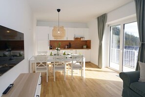 A modern kitchen with white cabinets, a dining table with chairs, and a hanging light fixture.