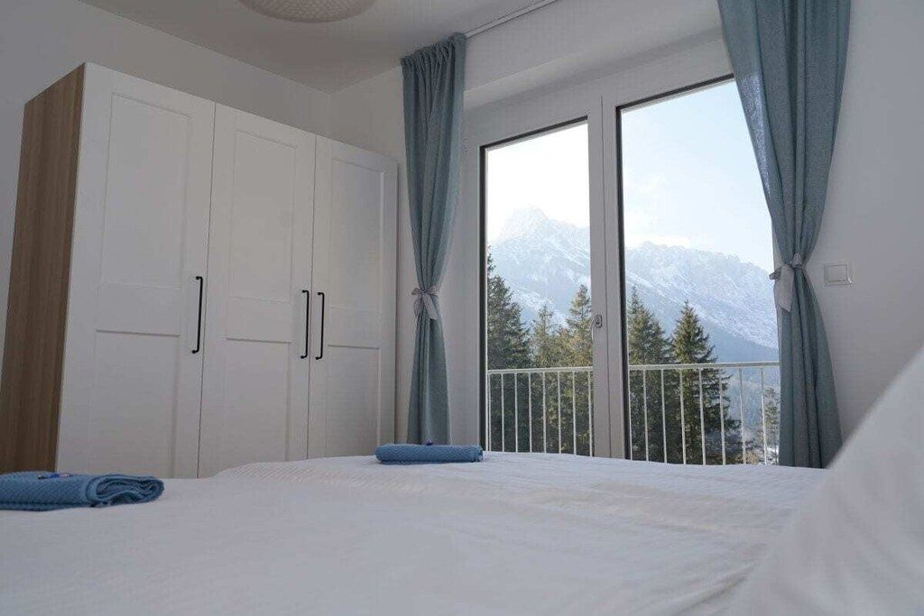 A bedroom with a large bed, a wardrobe, and a balcony with a mountain view.
